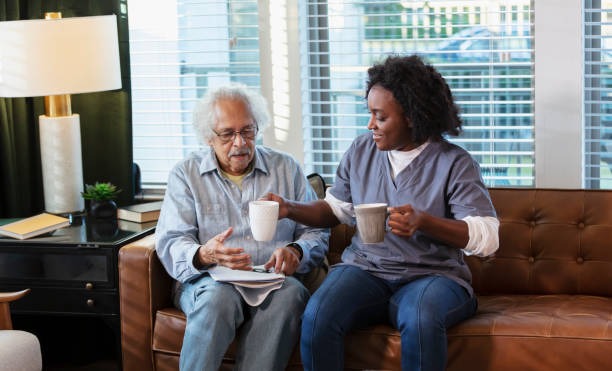 Home caregiver brings coffee cup to senior man on sofa