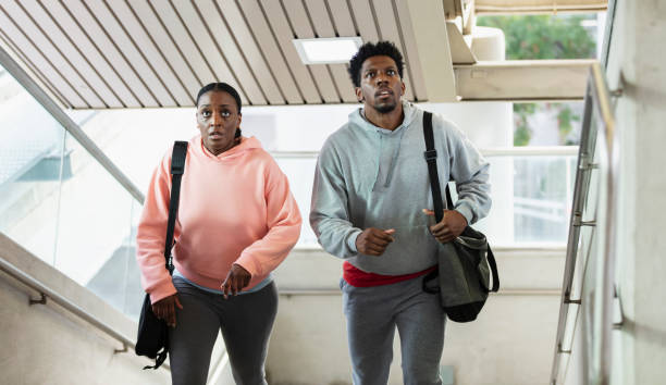 African-American couple climbing stairs, look lost An African-American couple in their 30s wearing casual clothing, carrying shoulder bags, climbing the stairs inside a public building. They look anxious or lost, not sure of where they are going. looking around stock pictures, royalty-free photos & images