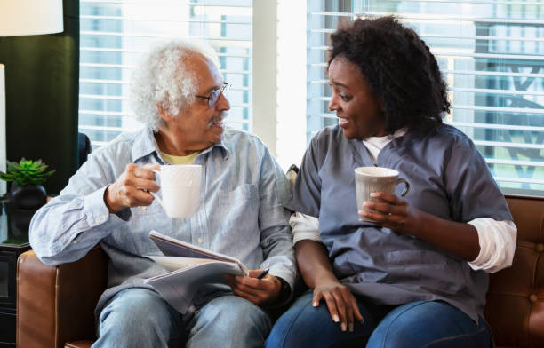 istock Home caregiver talks with senior man, sitting on sofa 1397411443