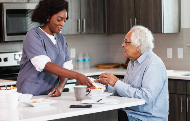 Home caregiver helps senior man in kitchen stock photo
