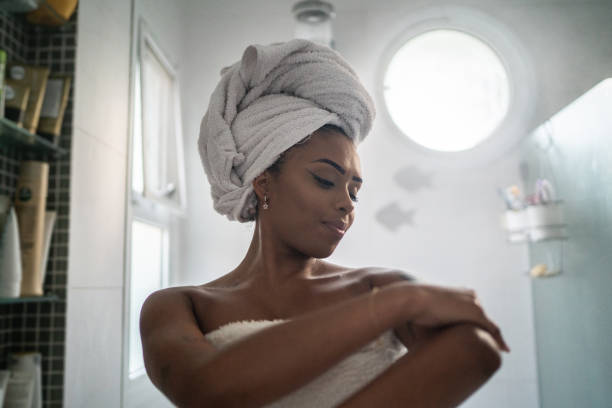 young woman applying moisturizer on the body after shower at home - vrouwelijkheid fotos stockfoto's en -beelden