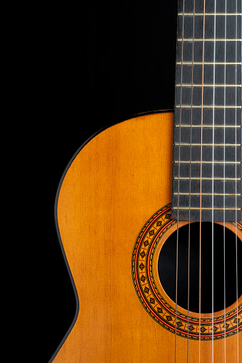 FRONT VIEW OF HALF OF A CLASSICAL SPANISH GUITAR ON BLACK BACKGROUND. COPY SPACE.