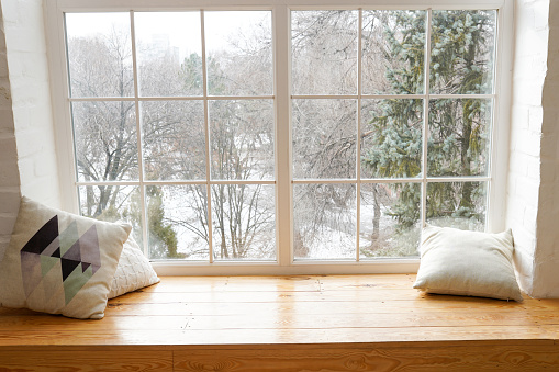 ozy and frost winter still life, white pillows on windowsill against snow landscape from outside