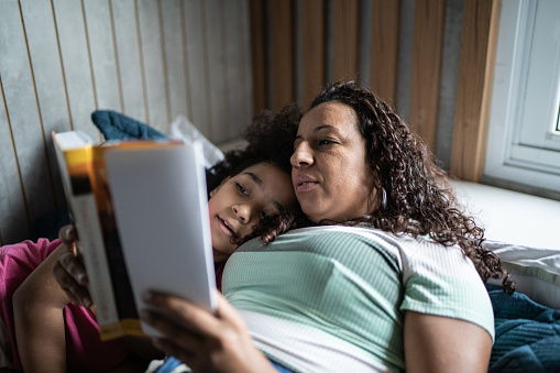 Mother reading a book to daughter in the bed at home