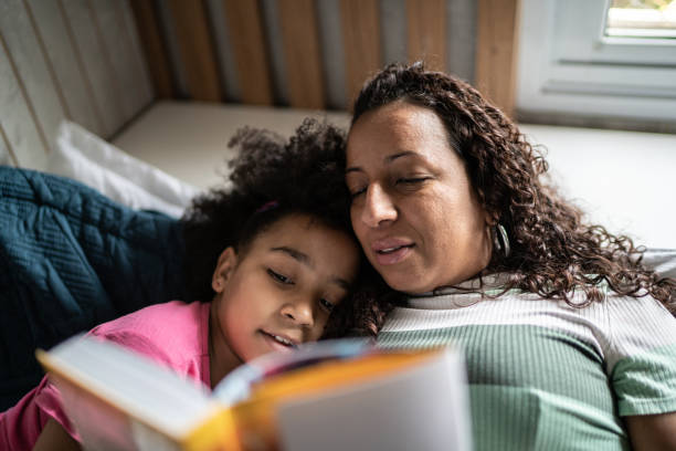 Mother reading a book to daughter in the bed at home