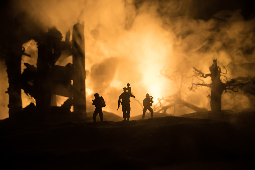 Silhouette soldier carrying little boy on his shoulder from fire. Rescue savior concept. Man moving out with little boy from burned out city destroyed in war. Selective focus