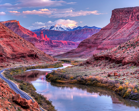 The Colorado River winds its way toward Fisher Towers glowing pink in the late afternoon Autumn light with the snow-capped La Sal Mountains behind near Castle Valey, Utah.