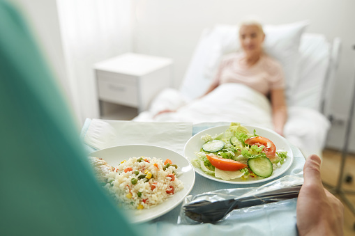 Person carrying tray with rice and vegetable salad to patient in bed of heath care center