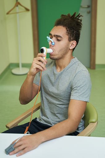 Male at the table with clip on his nose blowing air into mouthpiece of spirometer