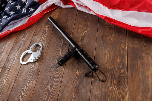 silver metal handcuffs and police nightstick near crumpled US flag on wooden surface