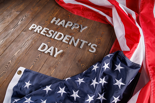 words happy presitdents day laid with silver metal letters on wooden surface near crumpled US flag