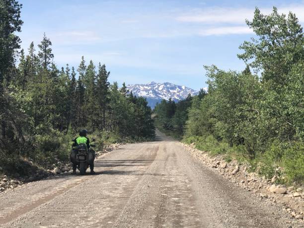 istock Lone motorcyclist on dirt road looking at mountain range in Canada 1397441215