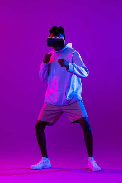 istock Young African man wearing VR glasses and interacting with virtual reality game in modern neon light studio background 1397444555