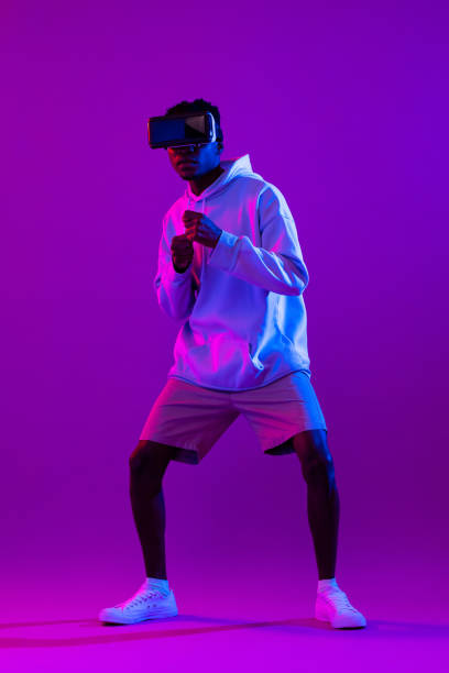 istock Young African man wearing VR glasses and interacting with virtual reality game in modern neon light studio background 1397444558