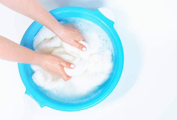 Female hands washing a white towels in basin, top view.