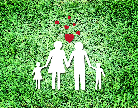 Top view with paper cut of family on grass with red hearts. Copy space for your design.