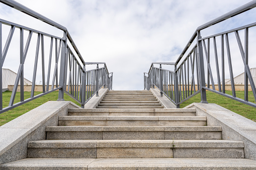 On the grass under the blue sky and white clouds, there is an empty staircase with guardrail