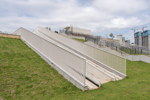 On the grass under the blue sky and white clouds, there is an empty staircase with guardrail