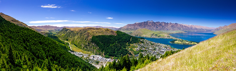 This November 2021 panoramic daylight image shows Tāhuna Queenstown, Aotearoa New Zealand. The top left shows Coronet Peak, a busy area for winter sports. In the centre left bottom, Gorge Road can be seen winding through the valley. On the centre right bottom, along the shores of Lake Wakatipu, is the city centre. The top right shows Tākitimu the Remarkables mountain range with a hint of snow. This image was taken on a sunny, spring day with mostly clear skies from near Ben Lomond Scenic Reserve.