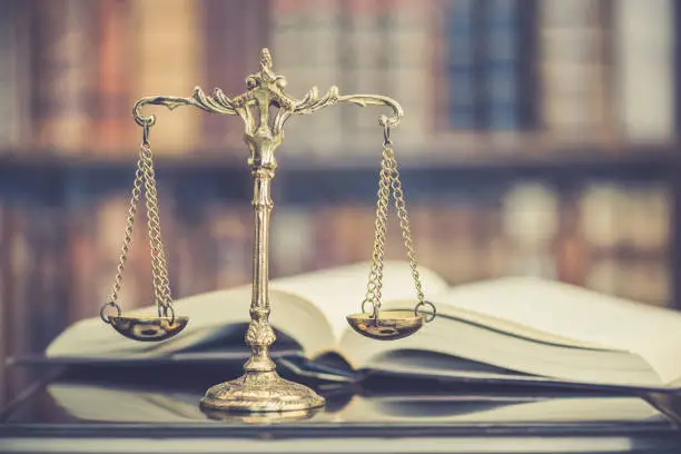 Photo of Legal office of lawyers, justice and law concept : Judge gavel or a hammer and a base used by a judge person on a desk in a courtroom with blurred weight scale of justice, bookshelf background behind.