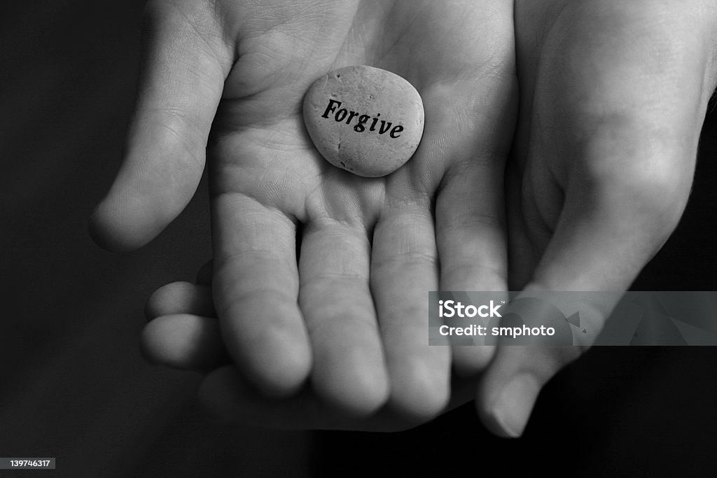 Two cupped hands holding a stone with forgive written on it Forgive stone offered in the palm of hand Forgiveness Stock Photo