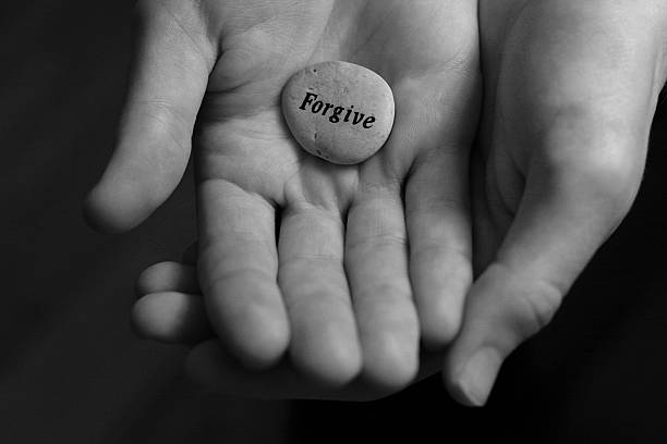 Two cupped hands holding a stone with forgive written on it Forgive stone offered in the palm of hand forgiveness stock pictures, royalty-free photos & images