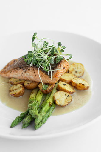 grilled salmon with asparagus, potato and butter sauce on white background
