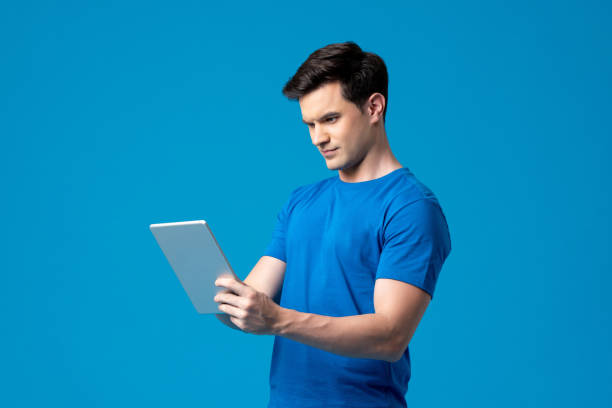 istock Young handsome Caucasian man holding tablet computer in isolated light blue studio background 1397466267