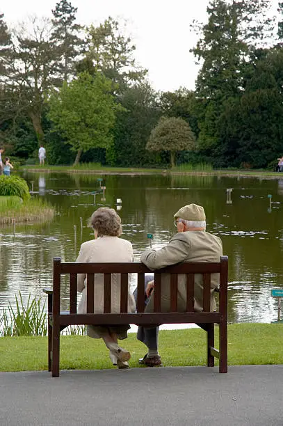 An elderly couple relax on a park bench.
