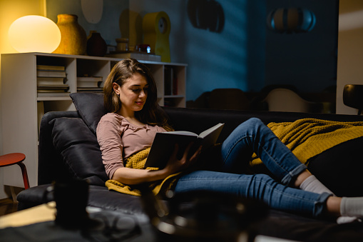 woman relaxing on a sofa and reading book at home.