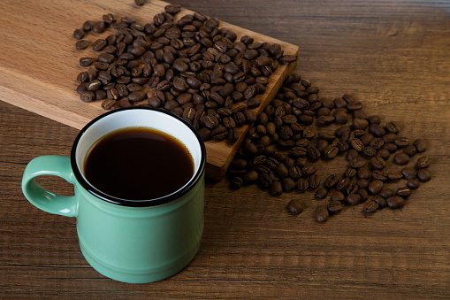 Green cup of coffee with coffee beans on wooden background
