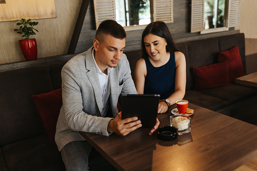 Young business couple having cup of coffee and using digital tablet in restaurant