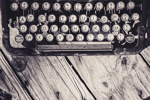 Old and weathered antique typewriter keyboard on wooden background in grayscale. Vintage and retro design.
