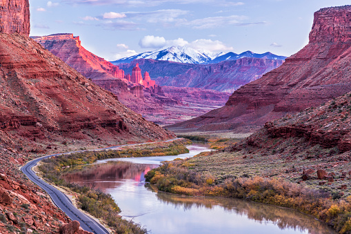 The Colorado River winds its way toward Fisher Towers glowing pink in the late afternoon Autumn light with the snow-capped La Sal Mountains behind near Castle Valey, Utah.