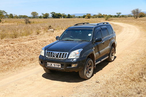 Lake Nakuru National Park, Kenya - February 1, 2021: Black offroad car Toyota Land Cruiser Prado 120 at a dusty road in an African savanna.