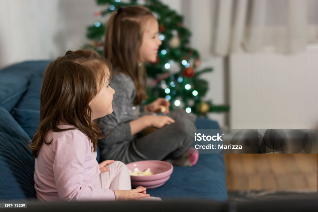 Children eating popcorn and wathcing movie Two girls seating in living room eating popcorn and watching tv during holydays Watching TV Stock Photo