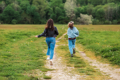 Family activity. A woman and a teen girl are joyfully running along a country road. Rear view. There is a forest in the background. The concept of freedom and happiness.