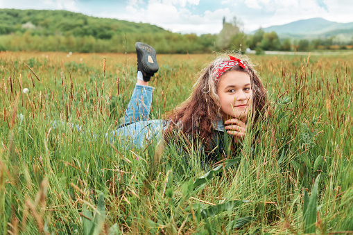 Portrait of pretty Caucasian teen girl lying on the field and looking at through the blades of grass. The concept of carefree, freedom and psychology.