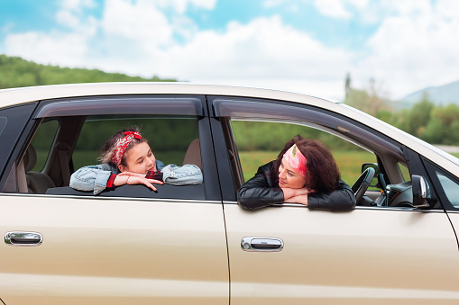 Travel and vacation. Smiling mother and daughter are sitting in the car and looking at each other. Side view. Copy space. The concept of purchase a new automobile.