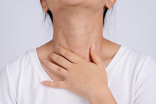 Woman holding her neck. She has a sore throat on a white background.