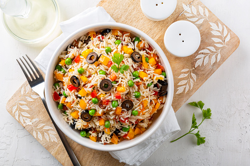 Rice Salad with fresh vegetables, bell bebber, tomato, green pea, black olives and olive oil,  on a white table. Directly above.