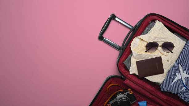 istock Open suitcase with sunglasses, camera, passport and clothes on pink background. Preparing for the summer vacations. 1397481054