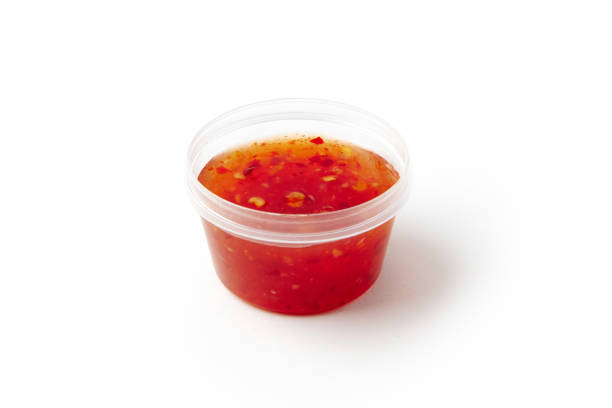 Sweet chili sauce in small plastic container isolated on white. Hot pepper condiment for food flavoring. Delicious handmade seasoning