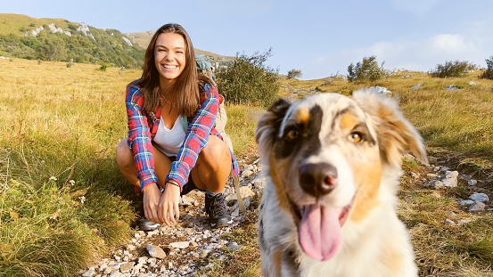 Portrait of young woman sitting with dog on grassy land against sky.