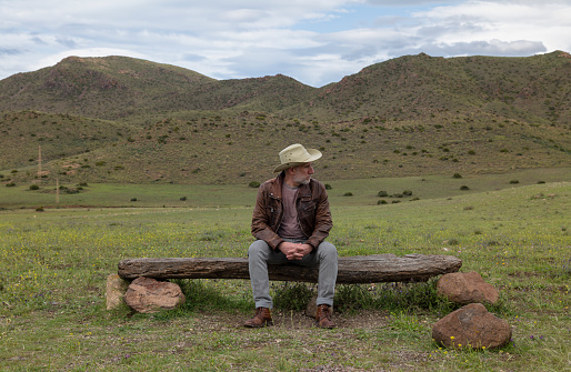 Adult man in cowboy hat sitting on wooden bench in field