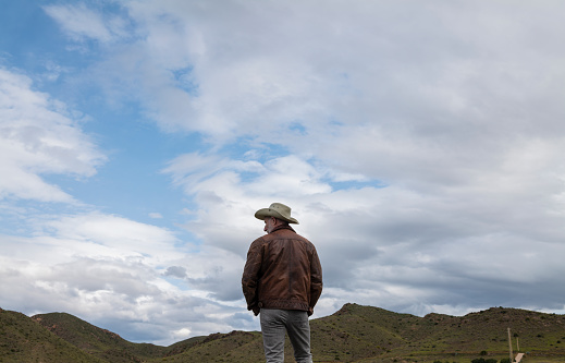 Rear view of adult man in cowboy hat on field against cloudy sky