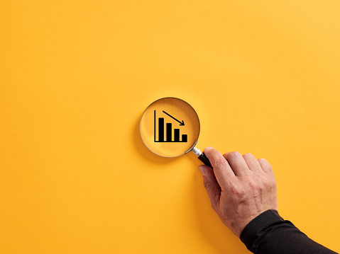 Hand holding a magnifier over the decreasing or descending graph. Economic crisis and financial recession concept.