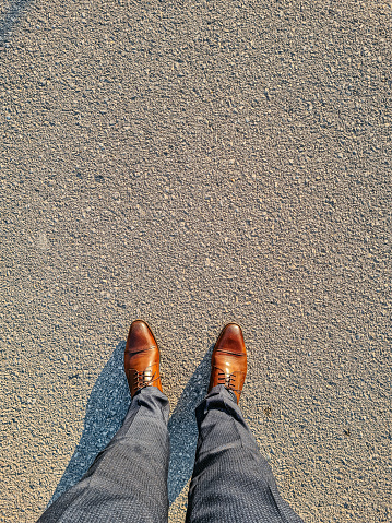 POV shot of a businessman in elegant brown shoes and suit pants walking forward on a concrete on a sunny day. Personal point of view directly from above.