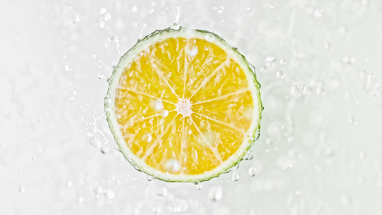 Close-up of half lime fruit in water against white background.