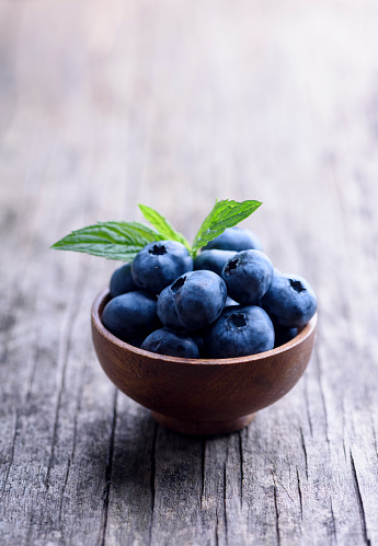 Bowl of fresh blueberries on rustic wooden table. Healthy organic seasonal fruit background. Organic food  blueberries and mint leaf for healthy lifestyle.